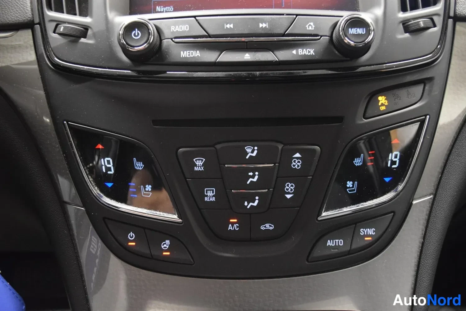 Muu: Lähikuva kojelaudan ilmastointipaneelista, jossa kaksivyöhykehallinta näytöillä 19 astetta sekä napit A/C, Auto, Sync, Max ja Rear.
