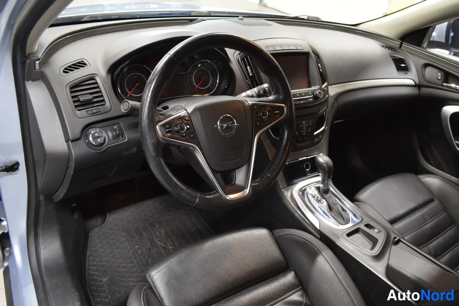 Muu: Ohjaamosta näkyy Opel-merkitty ohjauspyörä, mittaristo, automaattivaihteen valitsin ja mustat penkit.