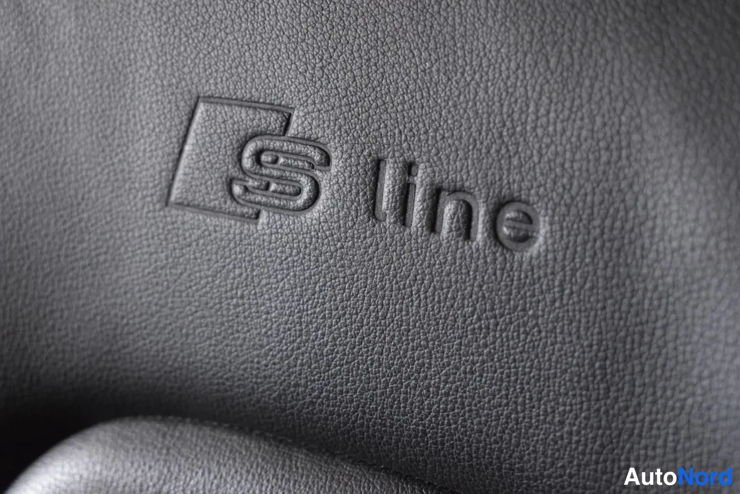 Yksityiskohta: Sivuperspective: tummanharmaan nahkapinnan kohokuvioitu S line -emblem lähikuvassa.