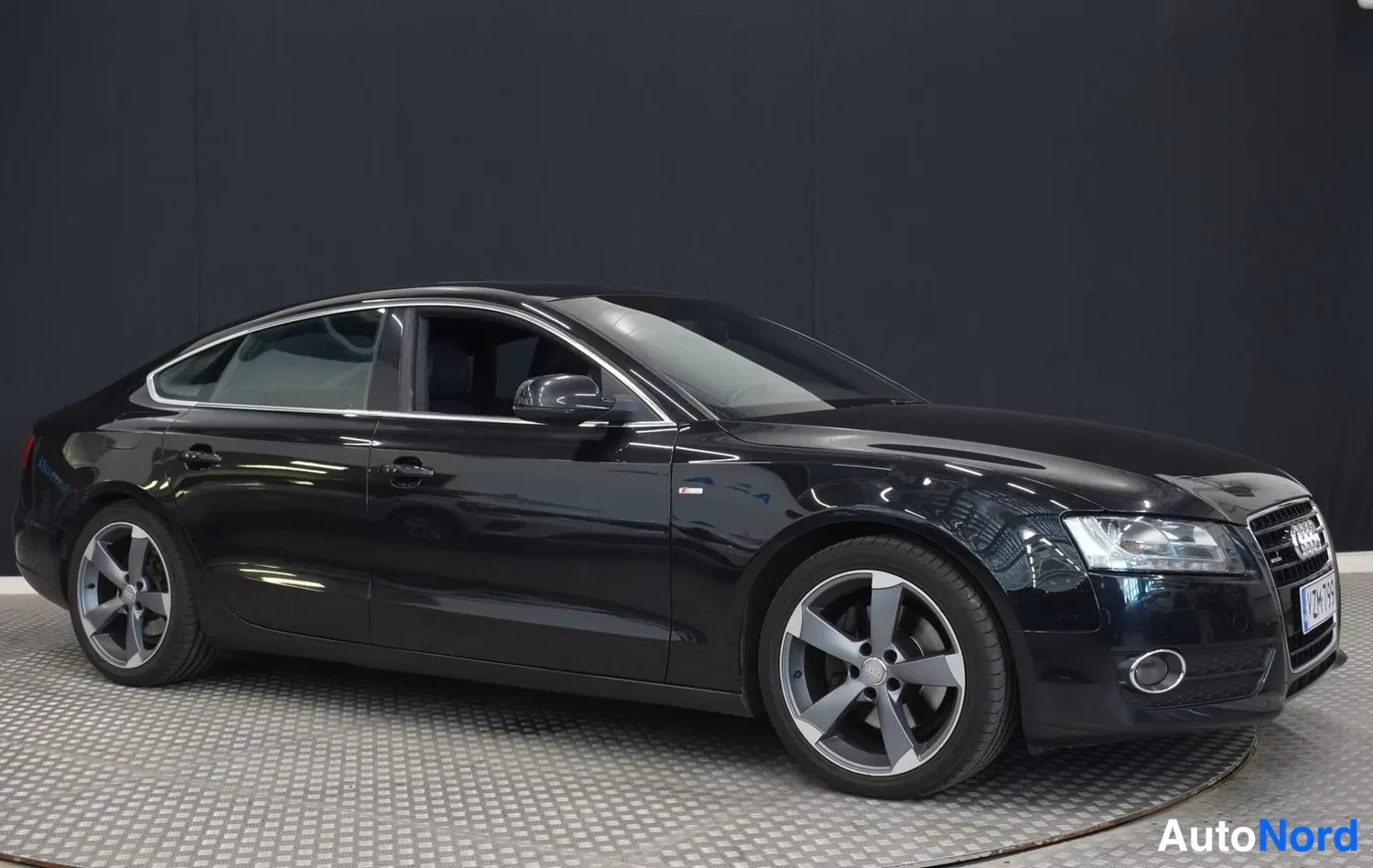 Etuviisto, nokka oikealle: Mustan Audi A5 Sportbackin etukulma, josta näkyvät etupuskuri, ajovalot ja kylki.