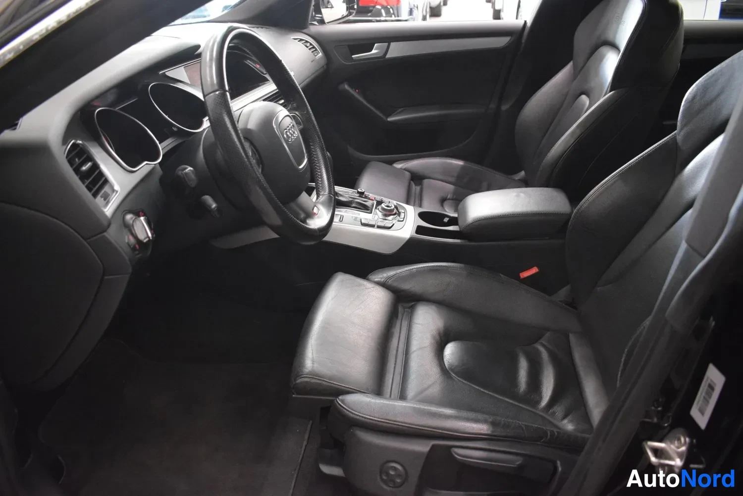 Etuviisto, nokka oikealle: Audi A5 Sportbackin etupenkkitila kuljettajan ovesta kuvattuna: mustat istuimet, ohjauspyörä ja keskikonsoli.