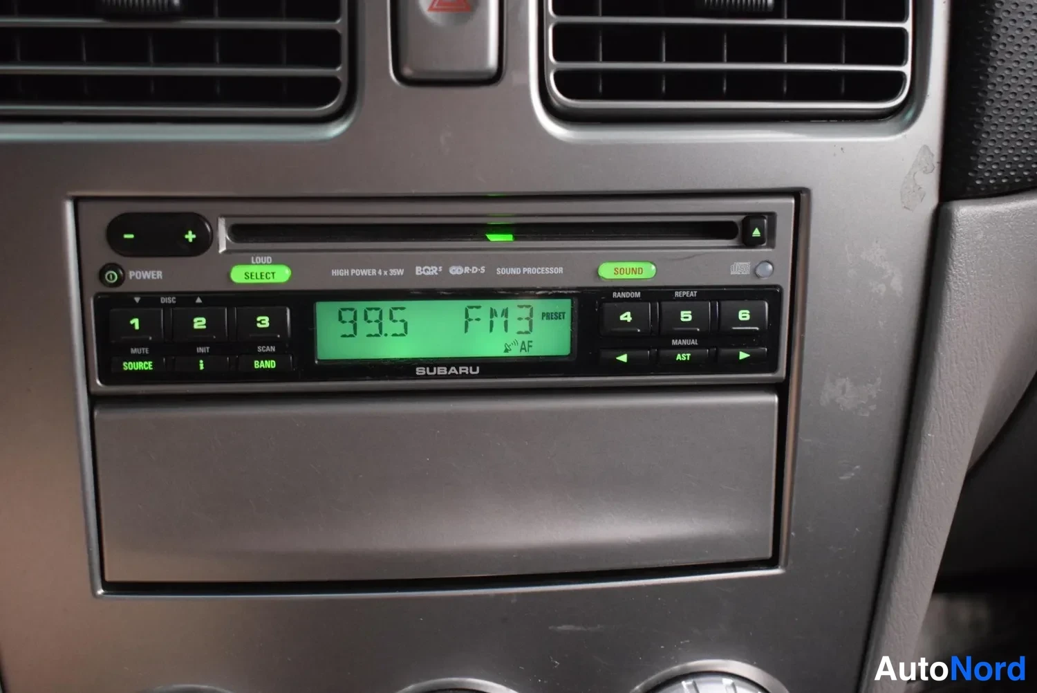 Yksityiskohta: Subaru-merkkinen radioidsensoija kojelautaan kiinnitettynä, näytössä 99.5 FM3
