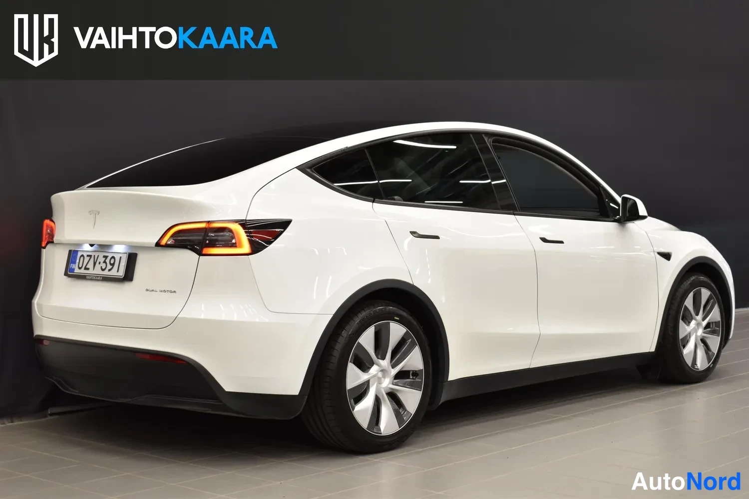 Takaviisto: Valkoinen Tesla Model Y takaosalta, perä ja rekisterikilpi näkyvissä vasemmalla.