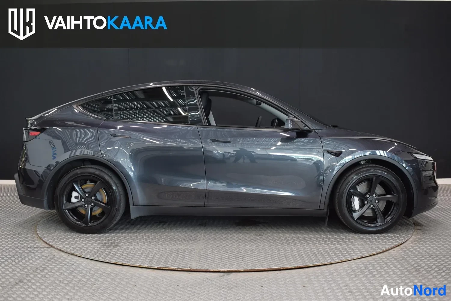 Sivulta: Tummanharmaa Tesla Model Y sivusta vasemmalta katsottuna studiossa.