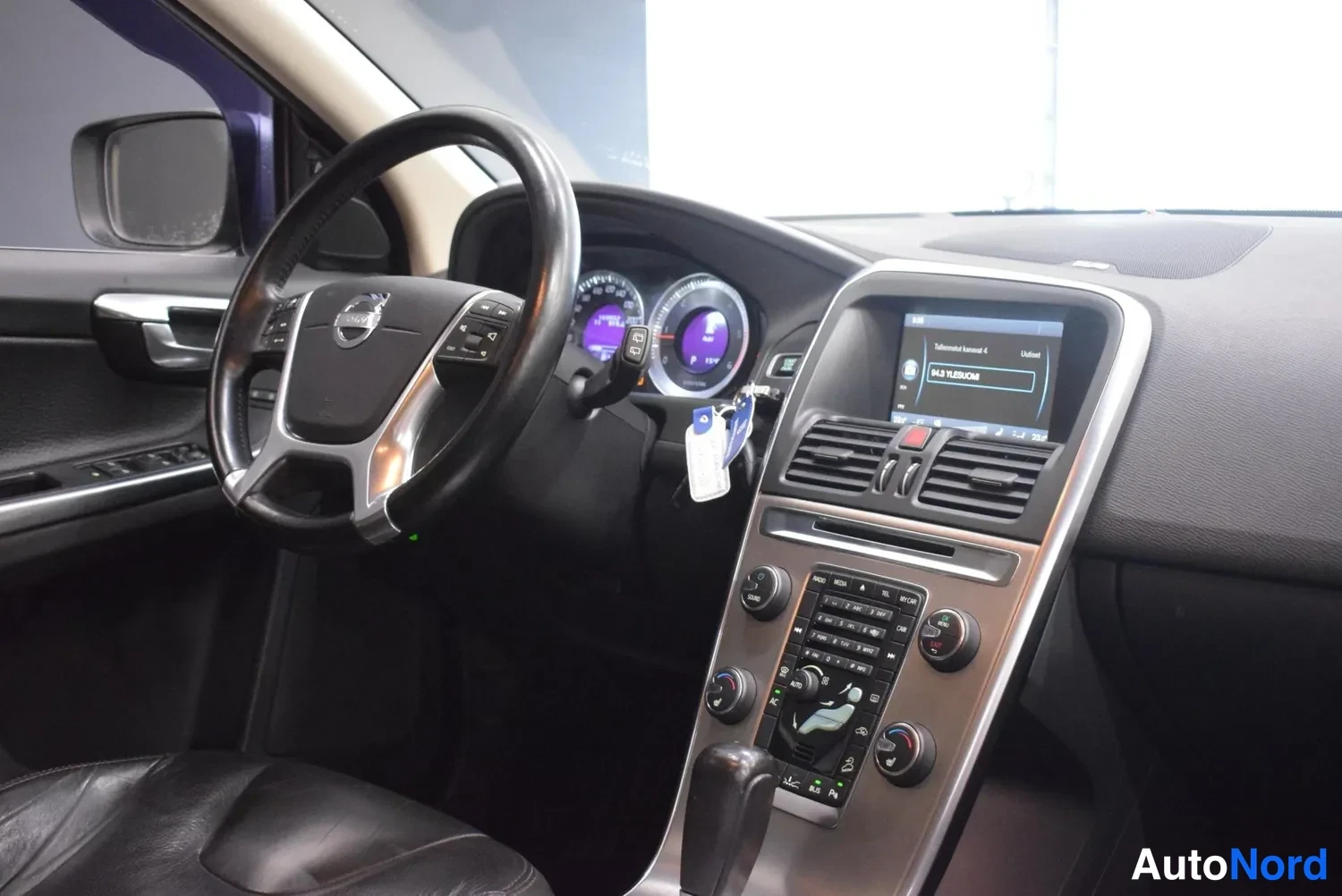 Yksityiskohta: Sisäkuva: Volvo-ohjauspyörä, mittaristo, keskikonsoli ja radio, vaihteenvalitsin näkyy.