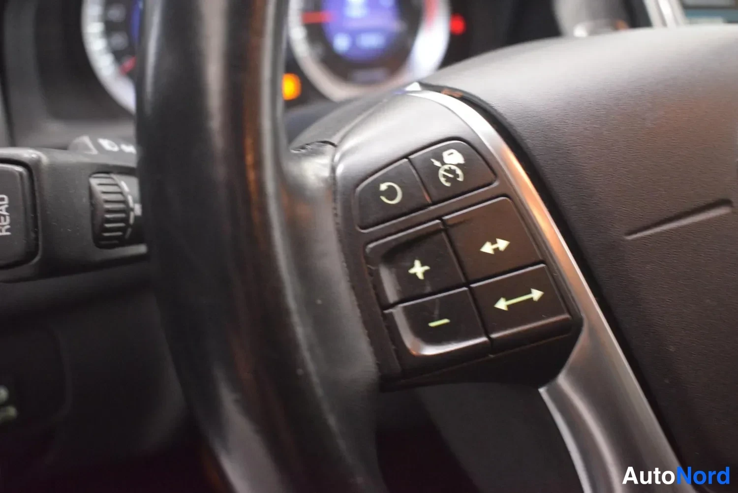 Yksityiskohta: Ohjauspyörän oikeanpuoleiset monitoimapainikkeet, joissa nuoli- ja cruise control -merkit, käsinoja sumeana.