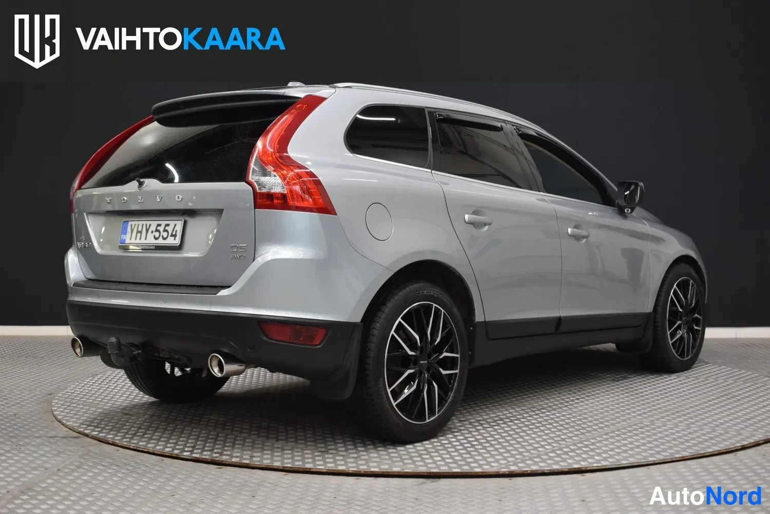 Takaviisto: Hopeanharmaan Volvo XC60:n takaokolikuskuva vasemmalta, rekisteritunnus, takakonttiin vedettävä vetokoulu näkyvissä.