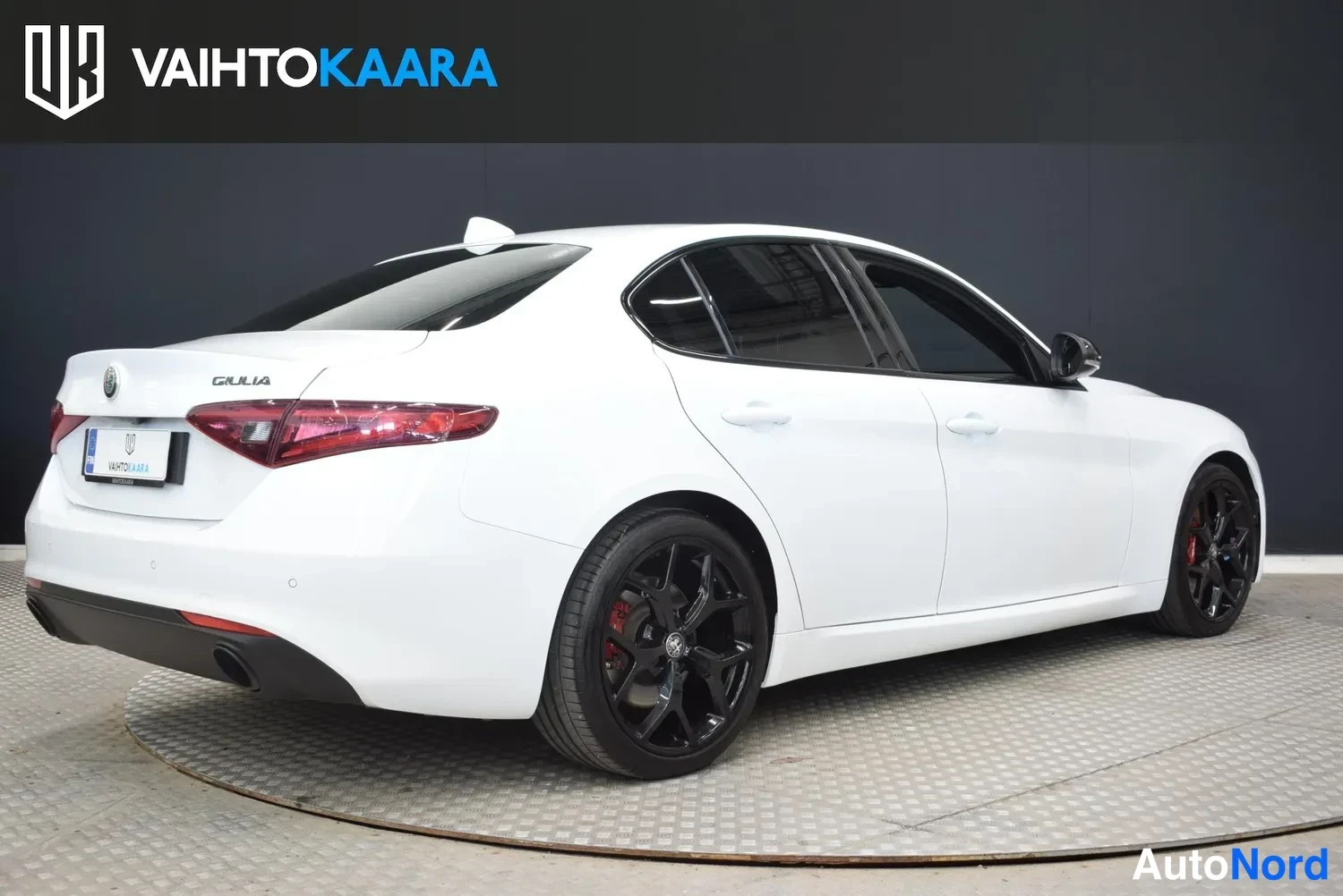 Takaviisto: Alfa Romeo Giulian takakulma toiselta sivulta: valkoinen koripinta, mustat vanteet punaisilla jarrustimilla, GUILIA-tunnus takaluukussa.