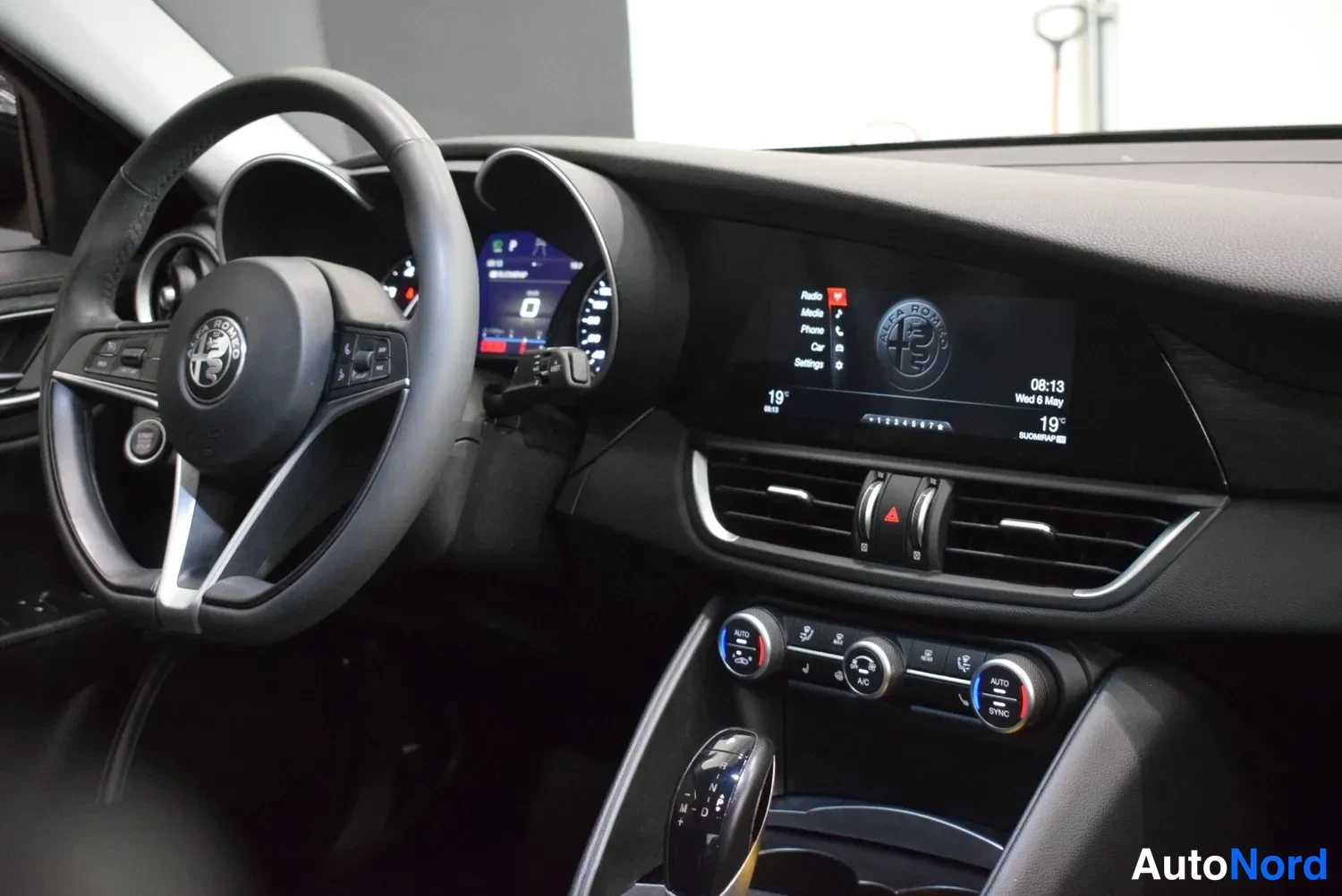 Muu: Ohjaamossa: Alfa Romeo -logollinen ohjauspyörä, näytöt ja ilmastointipaneeli näkyvät.