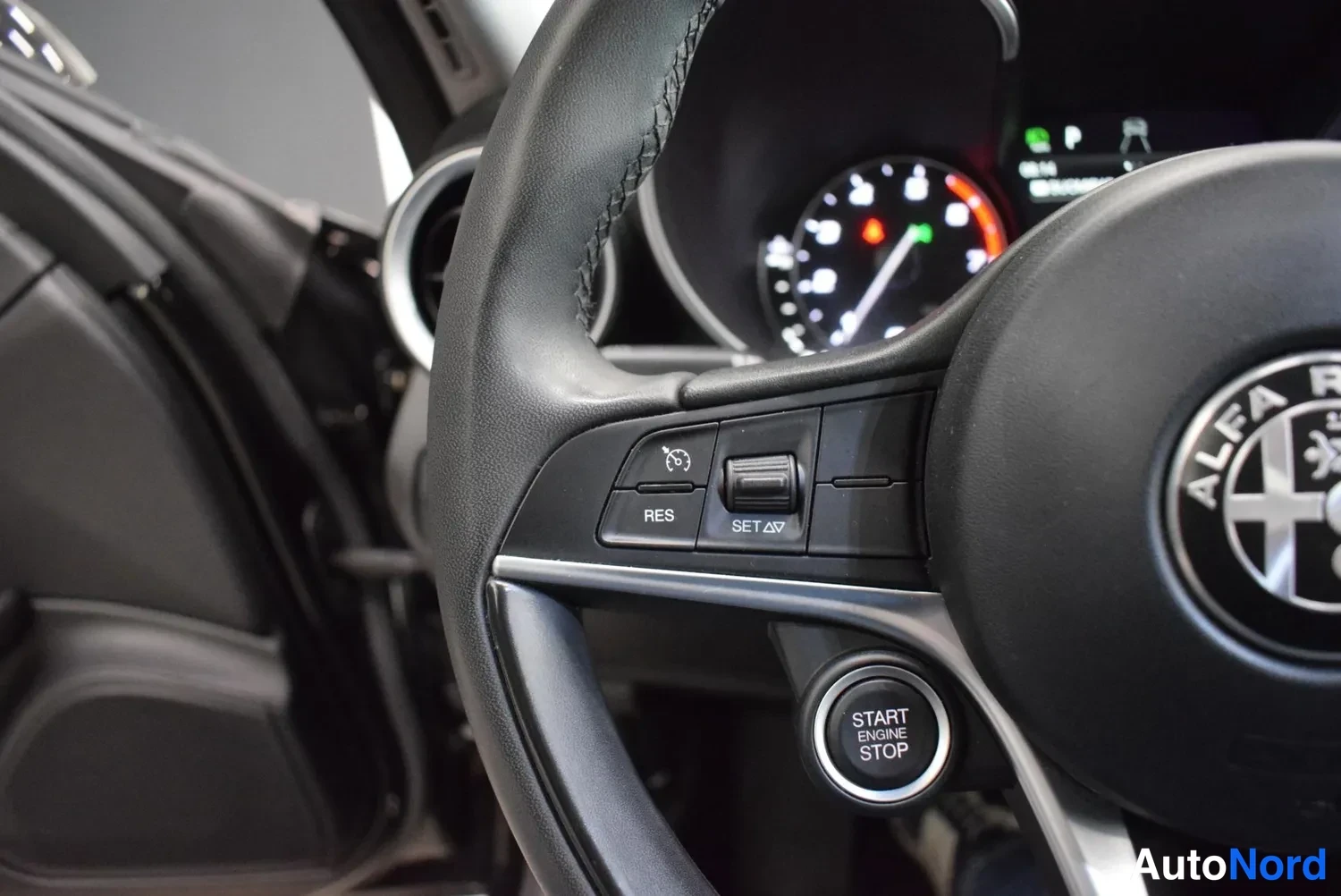 Edestä: Rattipainikkeet lähikuvassa: ristikkäiset RES- ja SET-merkit sekä START ENGINE STOP -painike.