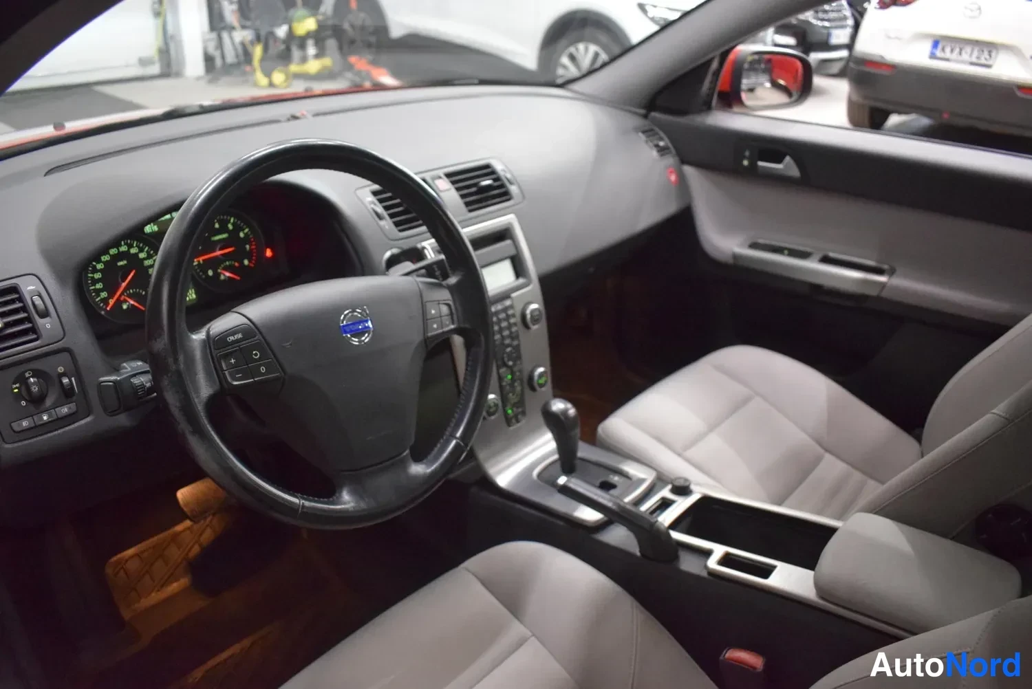 Muu: Volvo S40:n ohjaamosta: Volvo-merkkinen ohjauspyörä, mittaristo ja automaattivaihteen valitsin, etumatkustajan istuin kuvassa oikealla.