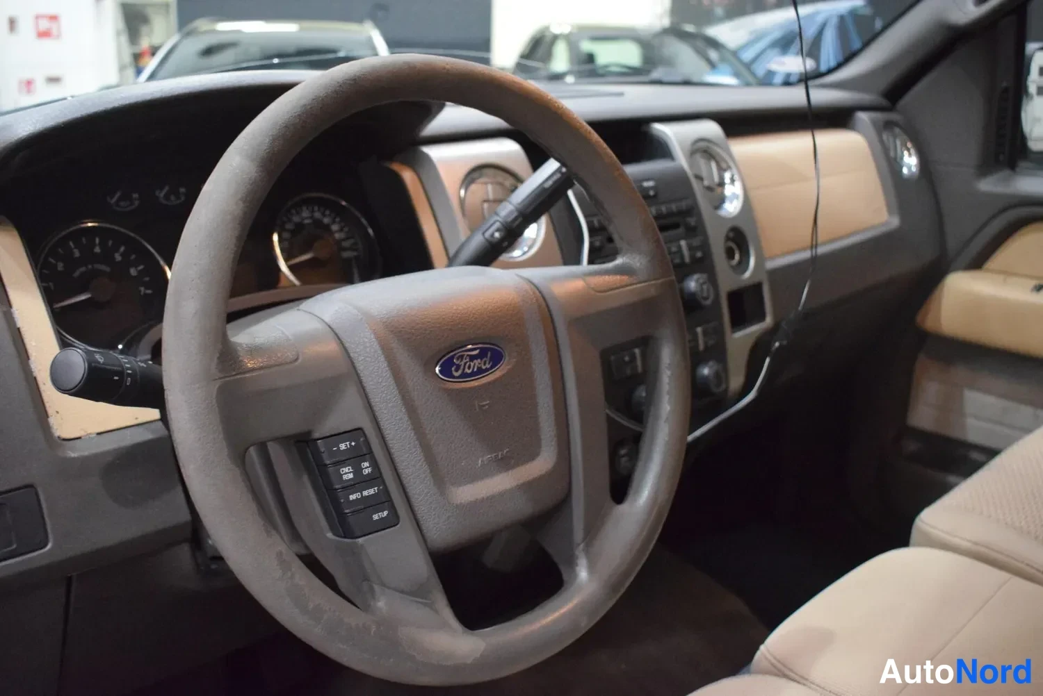 Sivulta: Lähikuva ohjauspyörästä ja kojelautasta: Ford-logollinen tumma ohjauspyörä, vakionopeudensäätimen painikkeet ('SET +', 'CNCL', 'RESUME', 'SET -'), analogiset mi