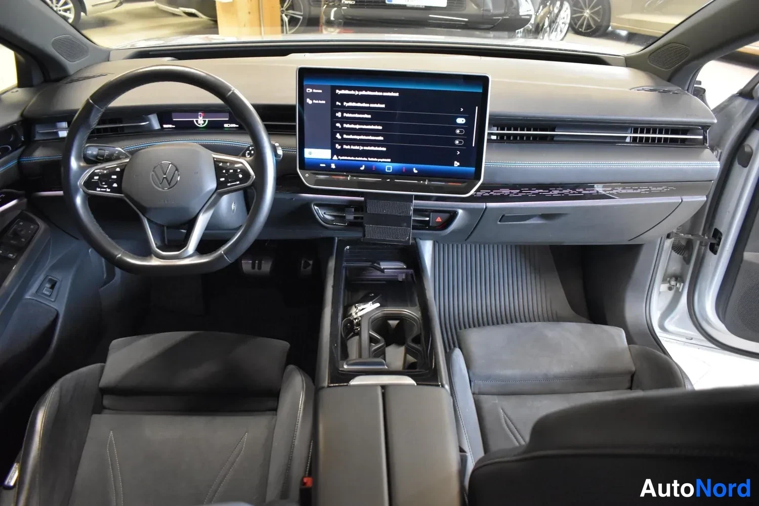 Muu: Sisätilakuva Volkswagenin ohjaamosta: ohjauspyörä ja keskellä suuri infotainment-näyttö, jossa on parkkihakuvalikko.
