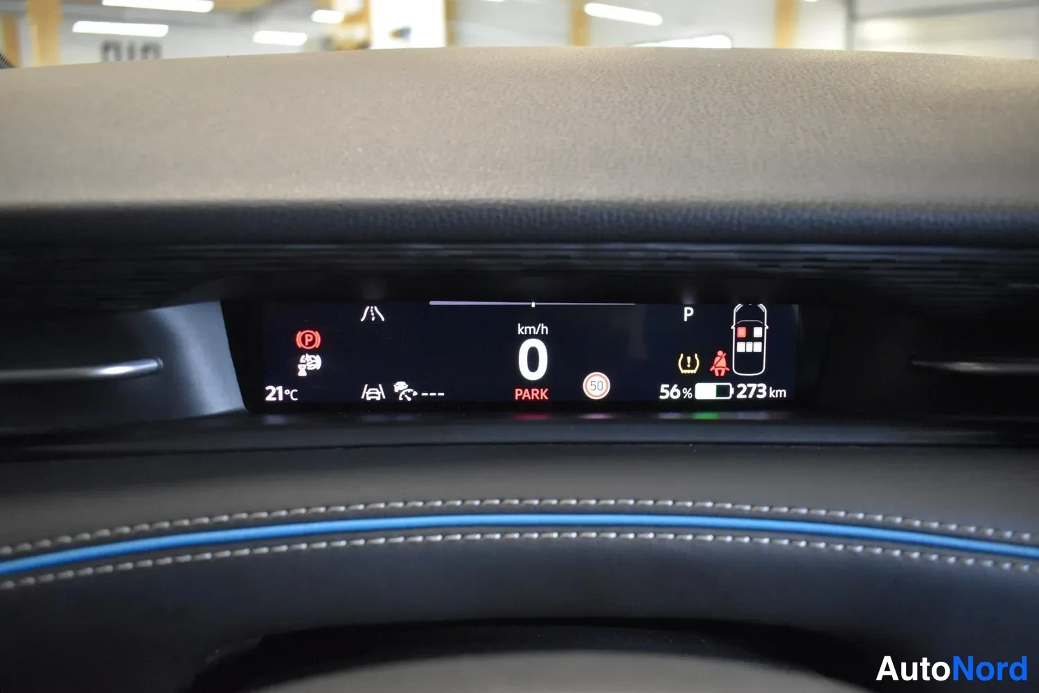 Muu: Sisätilakuva: kuljettajan näytössä lukee km/h, 0, PARK, 56 % akun varaus ja 273 km.