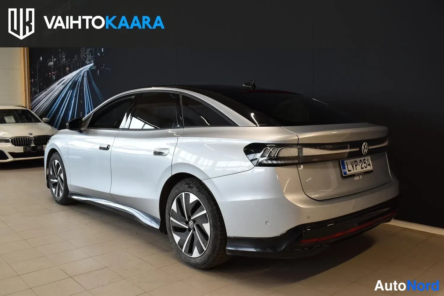 Takaviisto: Volkswagen ID.7 -sedanin takakulma oikealta, rekisterikilpi, hopea kori sisätiloissa.