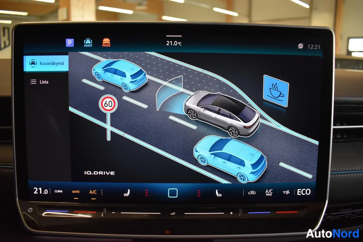 Yksityiskohta: Auton infotainment-näyttö, jossa näkyy IQ.DRIVE-assistentin kuva näkymä tienkäyttäjistä ja nopeusrajoituskilvestä 60, lämpötila 21,0 °C ja kellonaika 12:21.