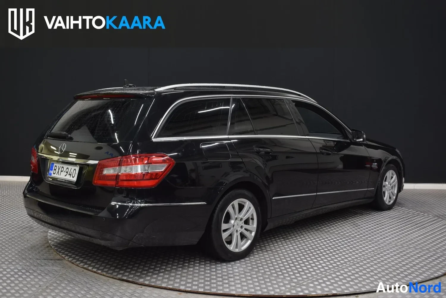 Takaviisto: Musta Mercedes-Benz farmari taka-kolmen neljäsosan näkymässä vasemmalta, rekisterikilpi ja tummat takaovet.