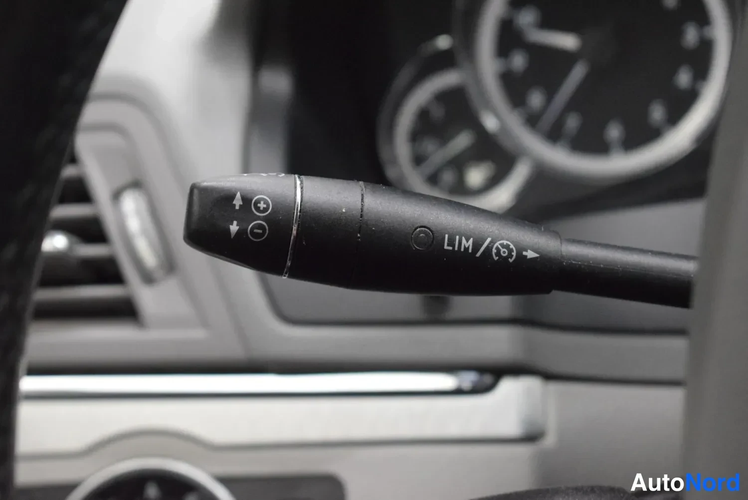 Muu: Vilkku- ja Ohjauspyörän takainen ratti- ja sipputoiminnon vipu, jossa merkinnät LIM ja Cruise Control -symboli; taustalla mittarit sumeana.
