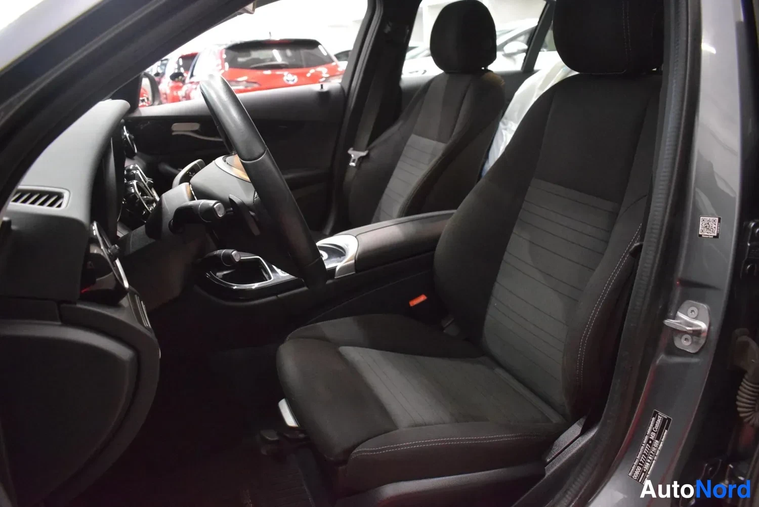 Muu: Mercedes-Benzin etumatkustamo ovelta kuvattuna: tummat kangasistuimet, ohjauspyörä ja keskikonsoli.
