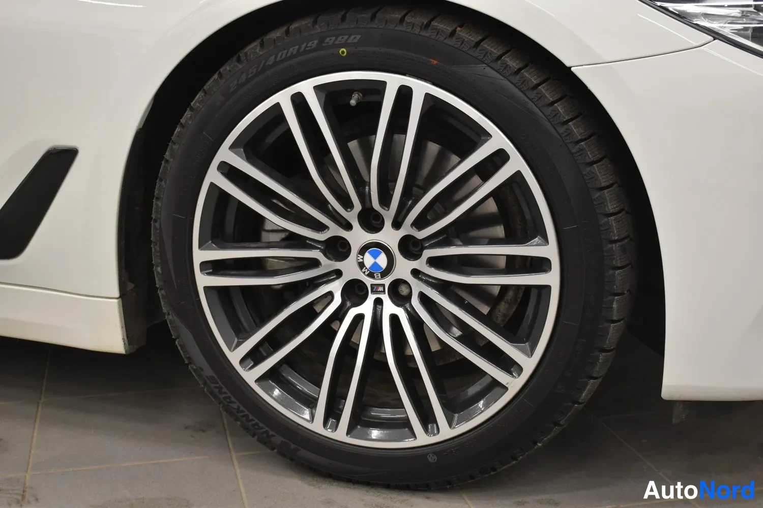 Sivulta: BMW-ympyrämerkillä varustettu monisakarainen kevytmetallivanne ja nokkarenengas lähikuvassa valkoisen auton kylkiosaan.