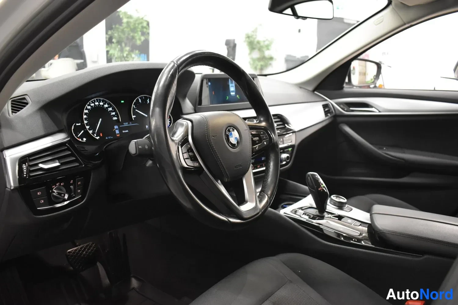 Muu: Kuljettajan näkymä tummasta ohjaamosta: BMW-ohjauspyörä, analogiset mittarit, keskimesta ja vaihteenvalitsin.