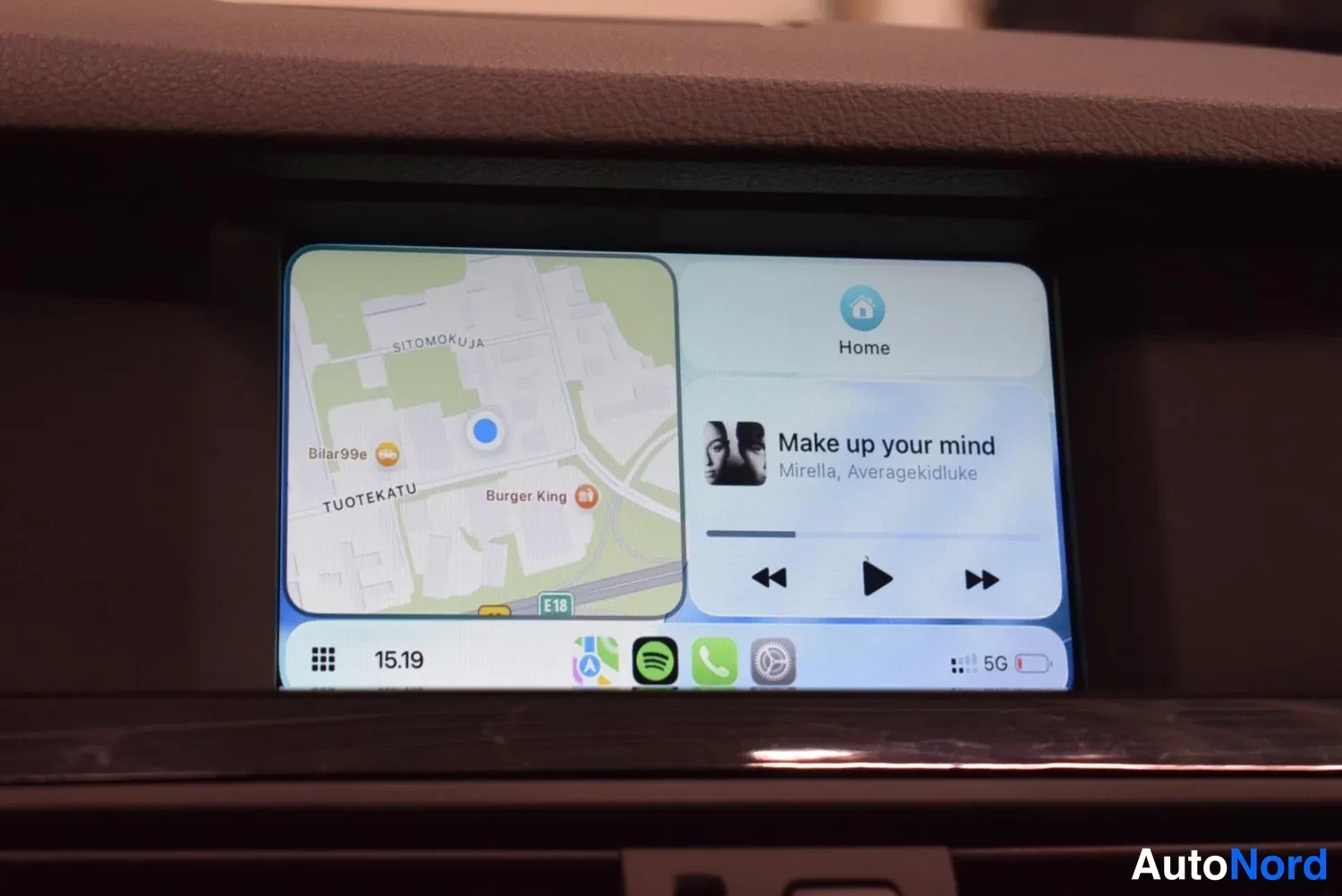 Yksityiskohta: Kojelautanäyttö näyttää karttaa ja musiikkisoittimen, jossa lukee 'Make up your mind' – Mirrella, Averagekidluke; alhaalla CarPlay-palkki ja kellonaika 15.19.