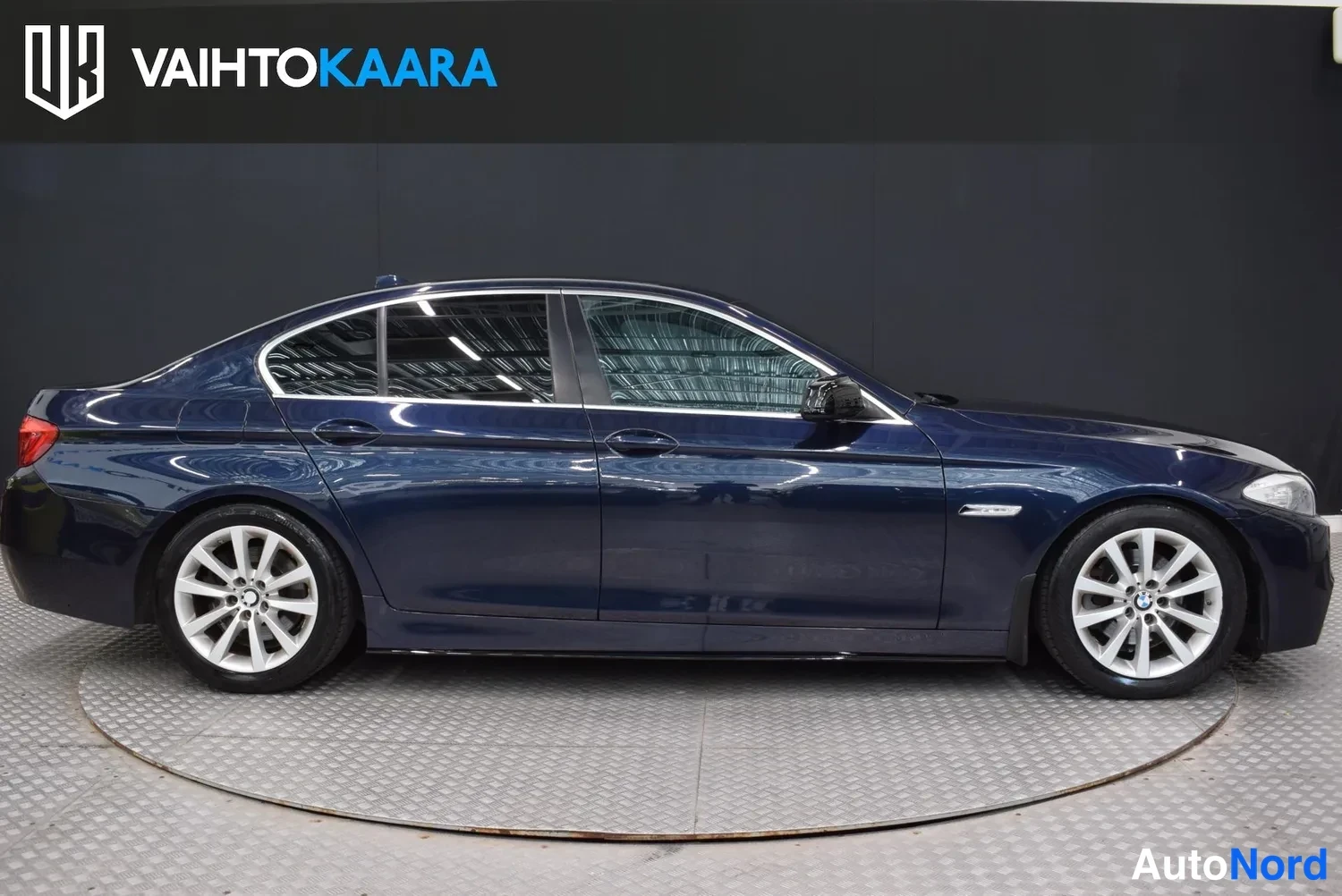 Sivulta: Sininen BMW -sedan sivusuunnasta kuvattuna kulmikkaalla lattialla tummaa taustaa vasten.