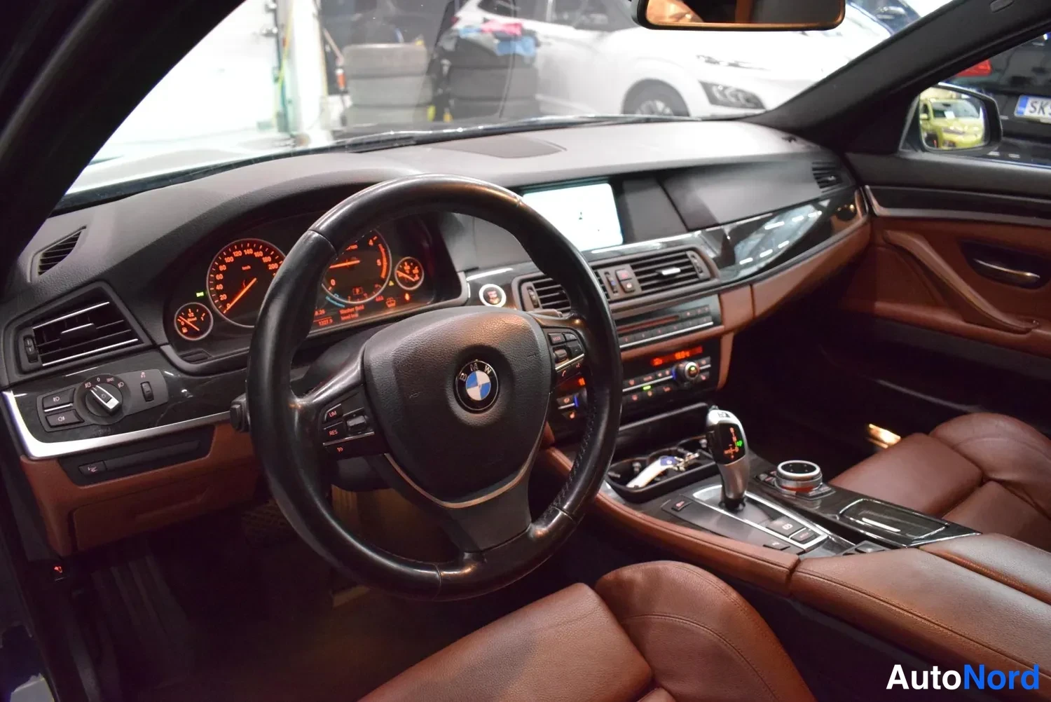 Muu: BMW:n ohjaamo: ruskeahkon nahkainen sisusta, ohjauspyörä, mittaristo ja keskiö konsoli vaihtajanäytöllä.