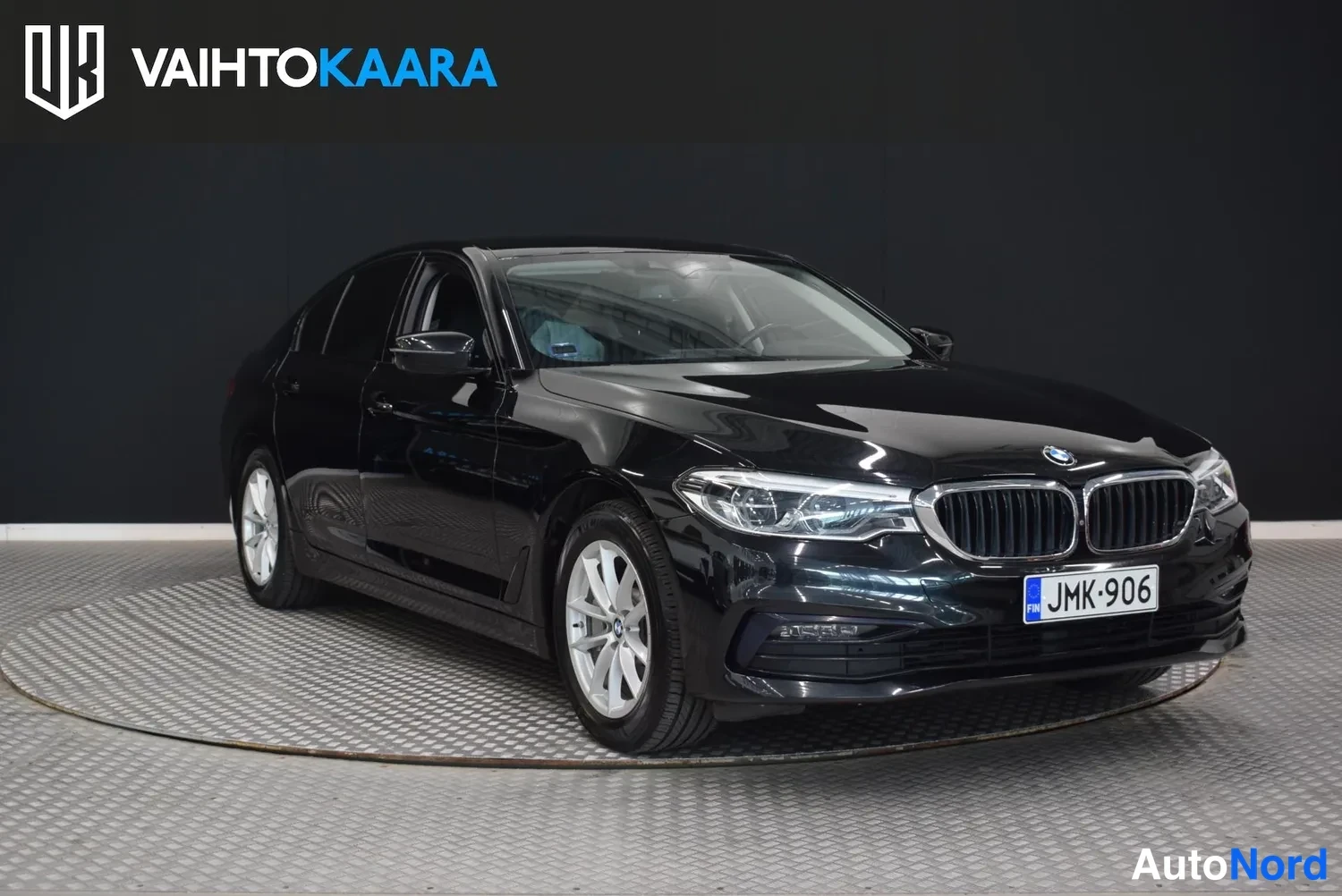 Etuviisto, nokka oikealle: Mustan sedanin etukulma, keulalla BMW-merkki ja rekisteritunnus, etupyörä ja kylki näkyvät studiossa.