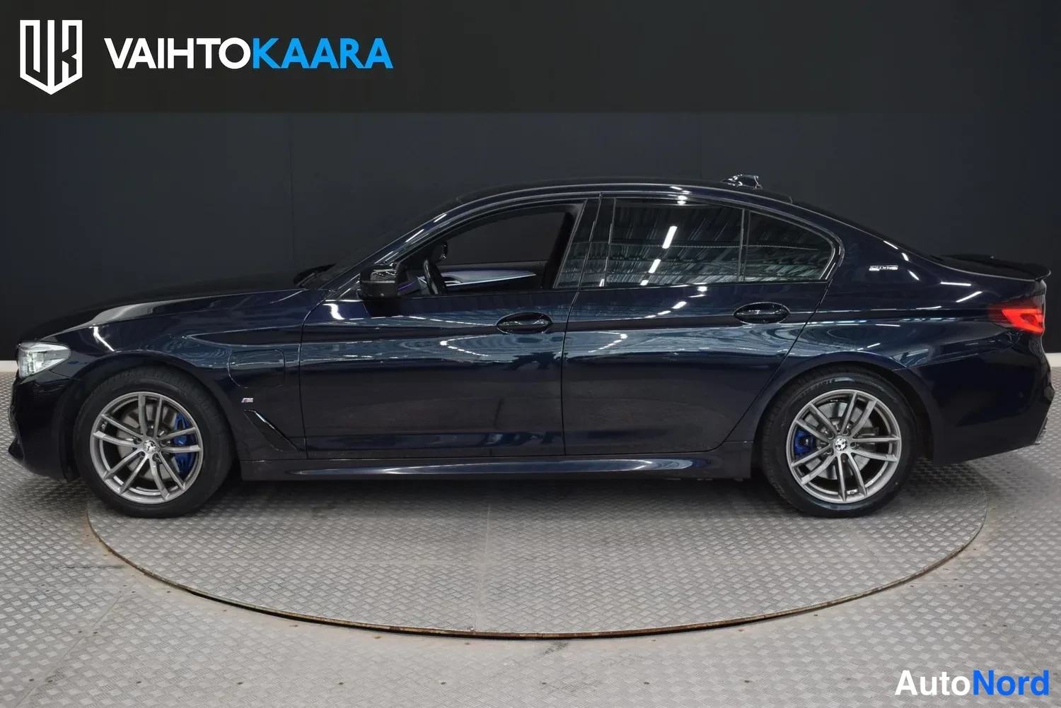 Sivulta: Sinimustan BMW-sedan vasen sivuprofiili studiovaloissa.