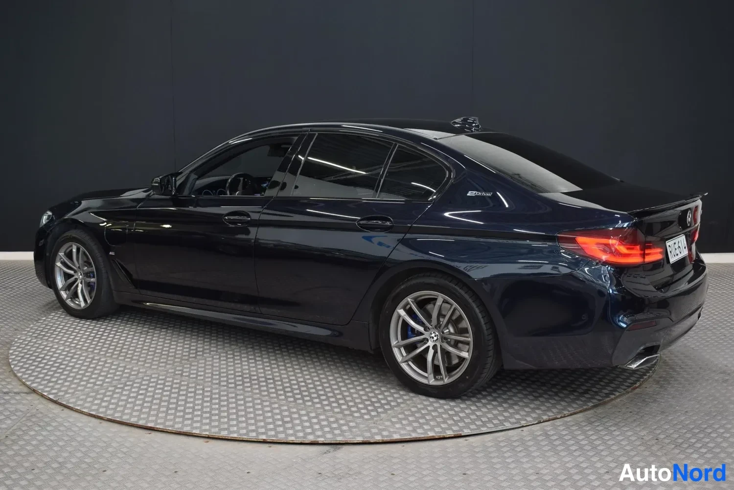 Takaviisto: Sinimustan BMW-sedan takaosa vasemmalta kolmivinkkaisesti studiovaloissa.