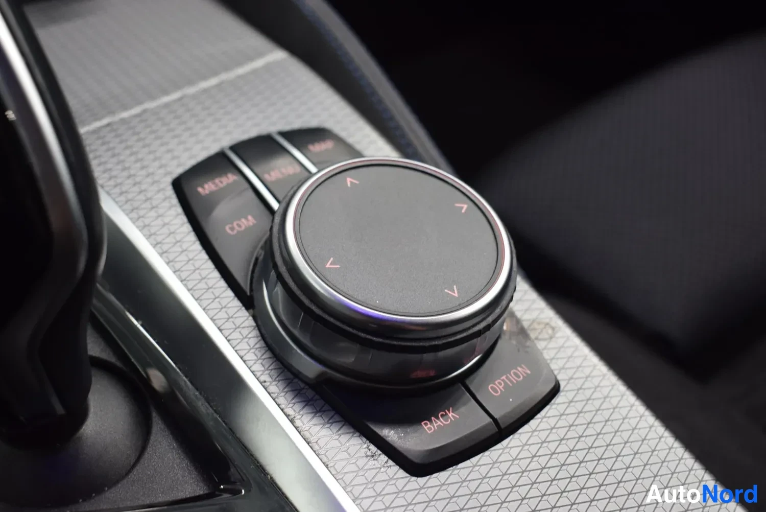 Yksityiskohta: BMW:n iDrive-ohjainkuppi ja sen ympärillä näppäimet MEDIA, COM, BACK ja OPTION keskikonsolissa.