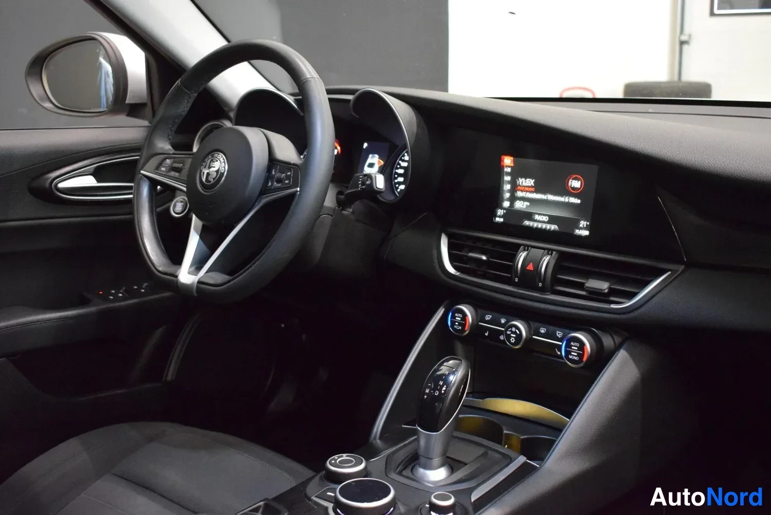 Muu: Kuljettajan näkökulma kojelautaan: Alfa Romeo -logollinen ohjauspyörä, kosketusnäyttö, automaattivaihteen valitsin ja ilmastointisäätimet.