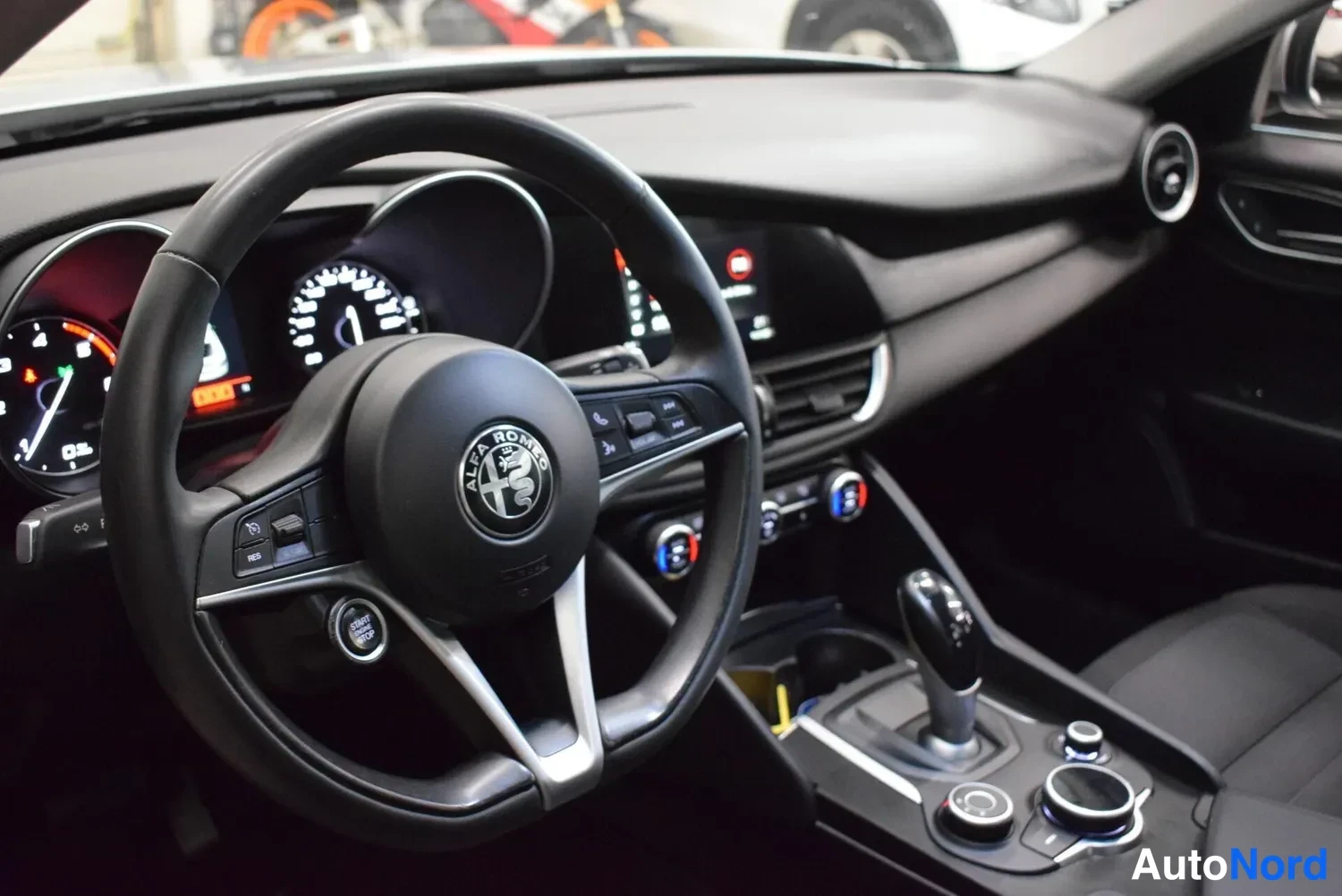 Etuviisto, nokka vasemmalle: Alfa Romeo-logollinen ohjauspyörä, mittaristo, kosketusnäyttö ja vaihteenvalitsin näkyvät tummasta sisätilasta.