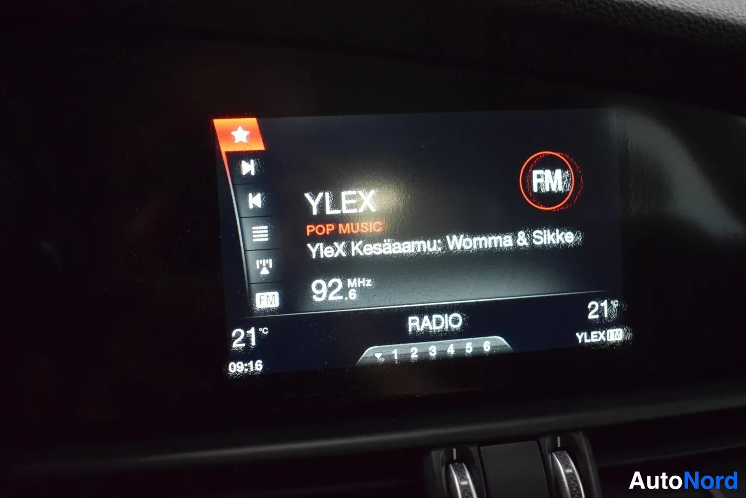 Muu: Auton radio-näyttö: YLEX-kanava 92,6 MHz, ohjelmassa 'YleX Kesäaamu: Womma & Silkke', kellonaika 09:16 ja lämpötila 21 °C.