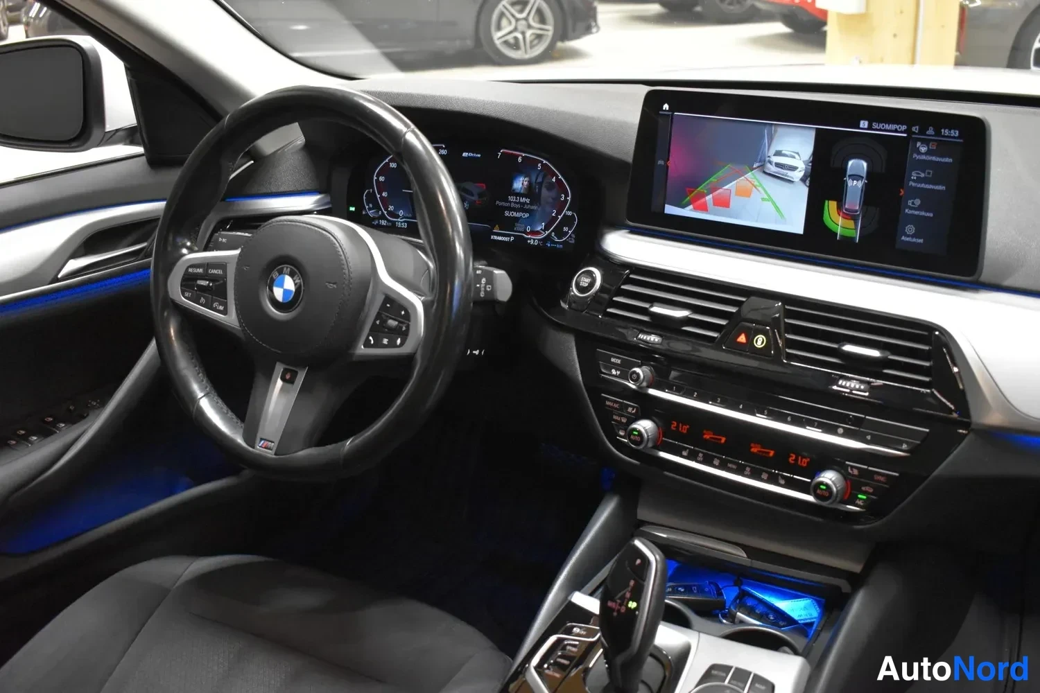 Muu: Kuljettajan näkökulma kojelautaan: BMW-ohjauspyörä, digitaalinen mittaristo, suuri kesk näyttö peruutus kameraluvulla ja ilmastoinnin säätimet.