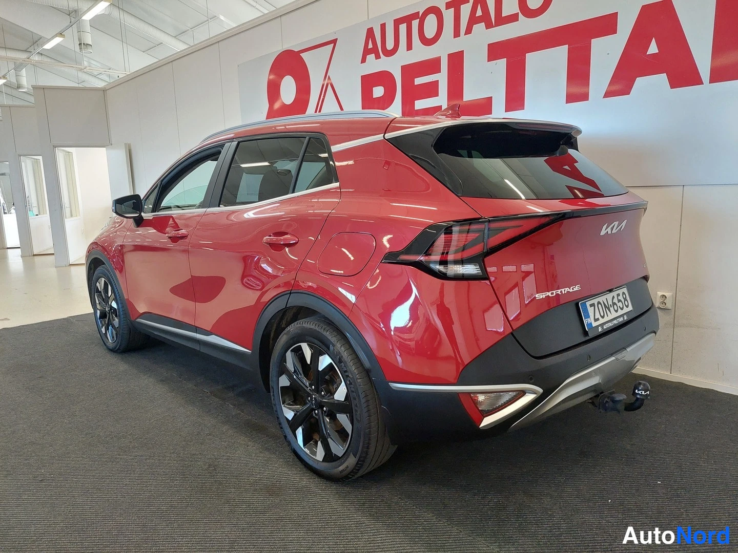 Takaviisto: Punainen Kia Sportage takaosa kolmannelta sektorilta sisätiloissa, rekisterikilpi, takavalo ja vetojavasen kiinnitys näkyvät.