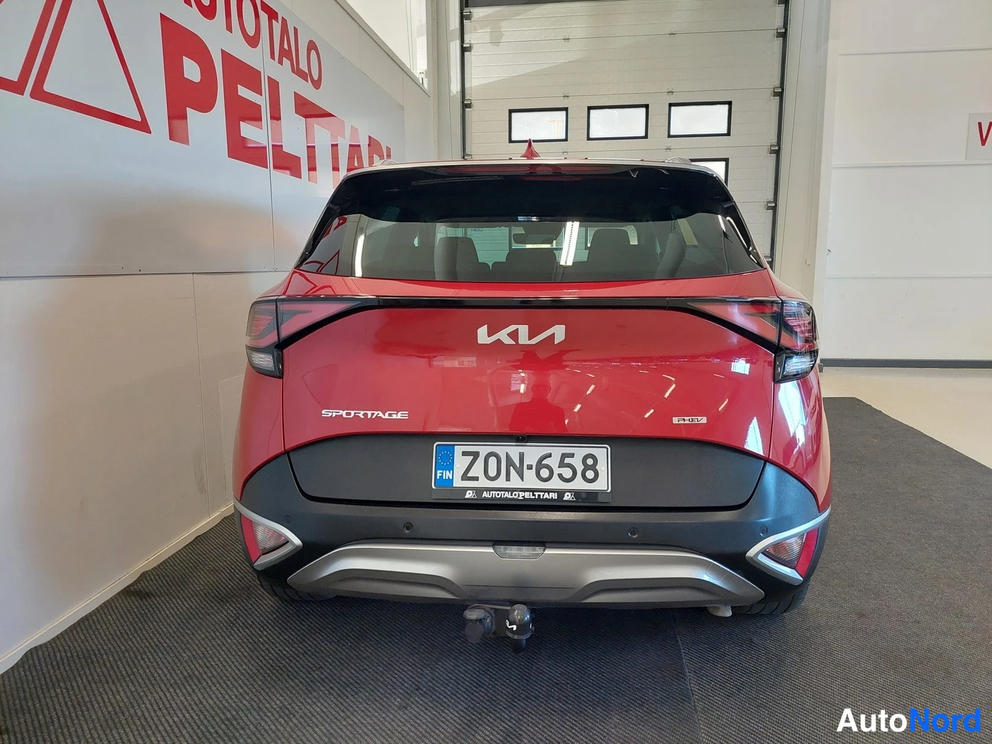 Takaa: Auton takaosa suoraan vastapäätä: punainen koripaneli, Kia-merkki, SPORTAGE-teksti, rekisterikilpi ja irrotettava vetokouluvarsi.