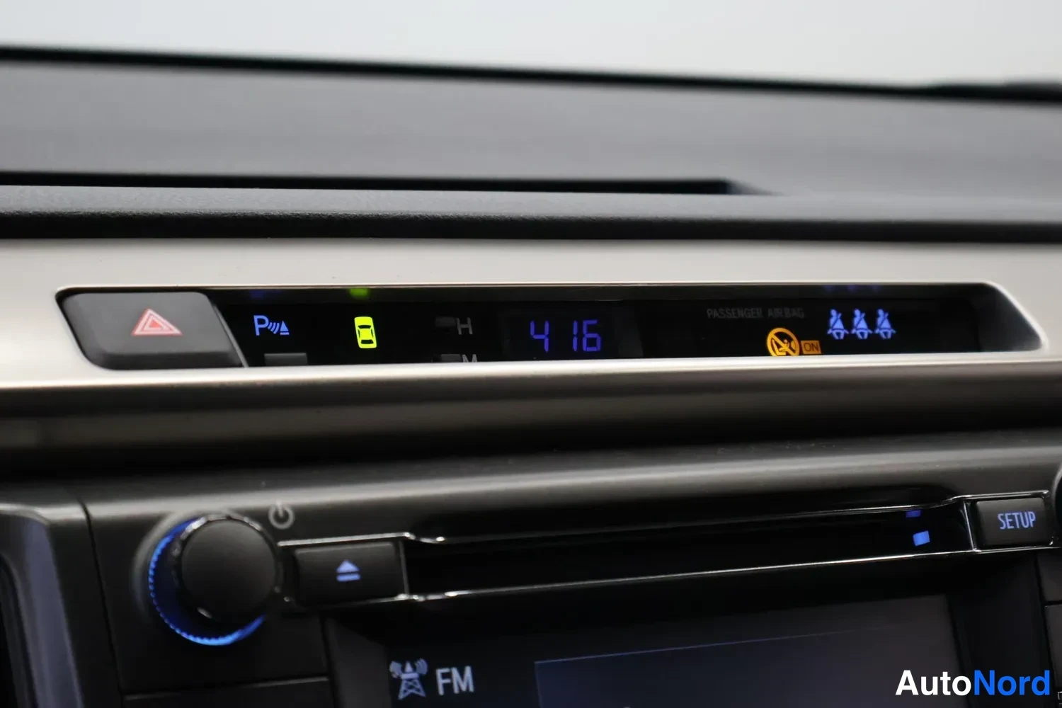 Yksityiskohta: Kojelaudan yläosan lähikuva, jossa näkyy sininen digitaalinen kello 4 16, P-merkinnäinen pysäköintitunnistinten kuvake, varoitusvalot ja radio-yksikön SETUP-nap
