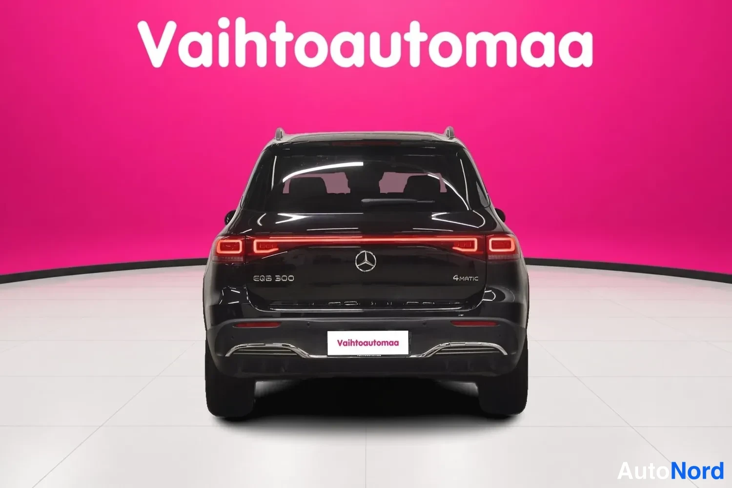 Takaa: Mustan Mercedes-Benz EQB:n suora takanäkymä: punainen poikittainen takavalo ja neljä ulos puhkeavaa parkkitutkan sensoria näkyvät pinkkiseinämää vasten.
