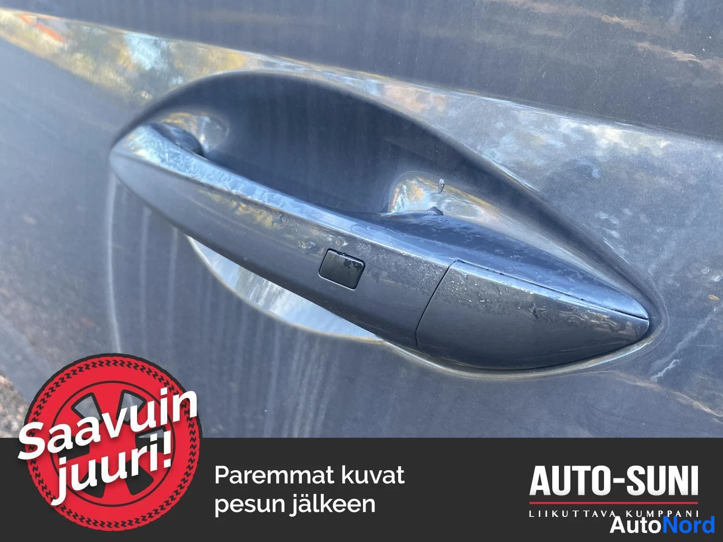 Yksityiskohta: Lähikuva auton ovenkahvasta, jossa pieni painike tummanharmaassa maalipinnassa.