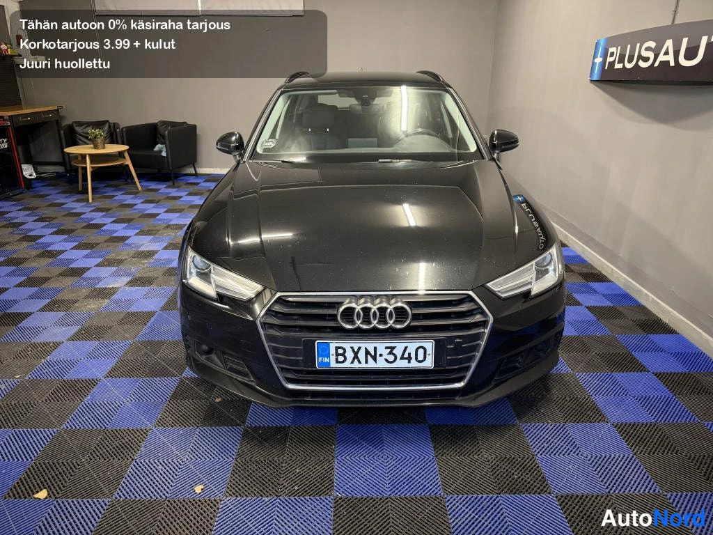 Edestä: Mustan farmariauton etukuva suoraan edestä, Audi-merkki konepellissä, rekisterikilpi.