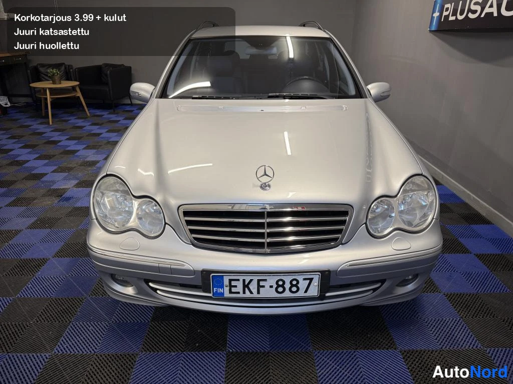 Edestä: Hopeinen Mercedes-Benz -auto suoraan edestä kuvattuna, konepelti, etusäleikkö ja kaksoisajovalot näkyvissä, rekisterikilpi.