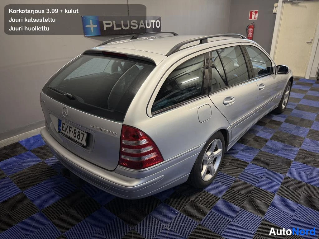 Takaviisto: Mercedes-Benz C-klassin farmarin takakulma vasemmalta ylhäältä kuvattuna sisätiloissa; hopeinen koripinta, takapuskurit ja kattotelineet näkyvät.