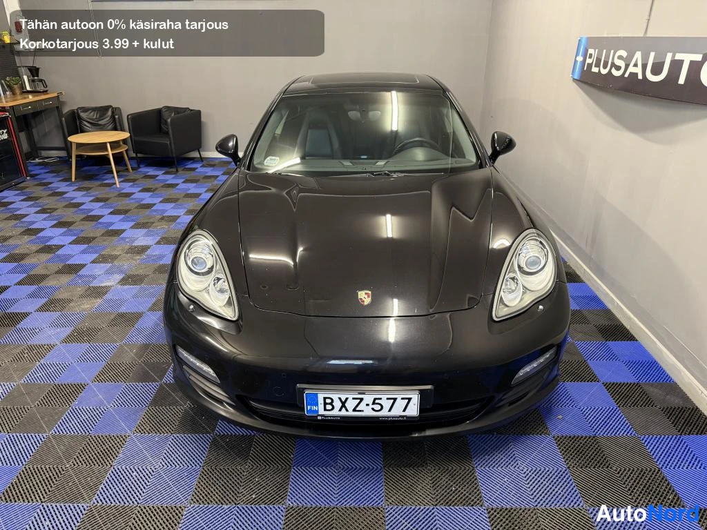 Edestä: Musta Porsche Panamera suoraan edestä, konepelti, ajovalot ja rekisteri näkyvät.