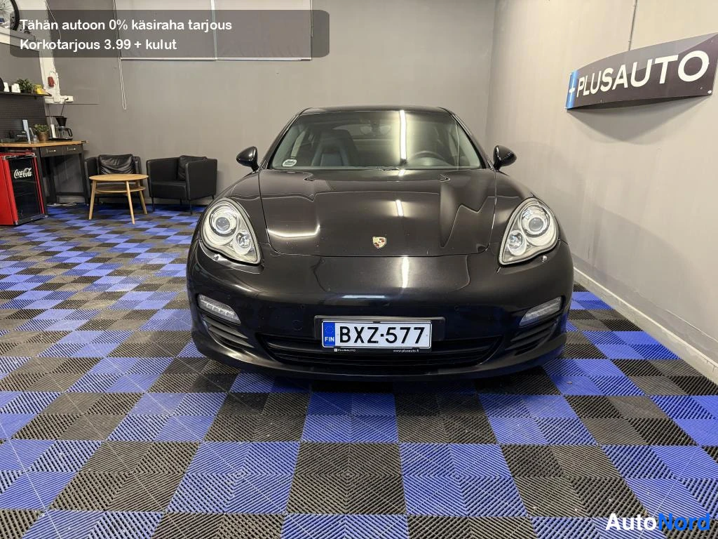 Edestä: Mustan Porsche Panameran etupää kohti kameraa showroomin lattialla, rekisterikilpi.
