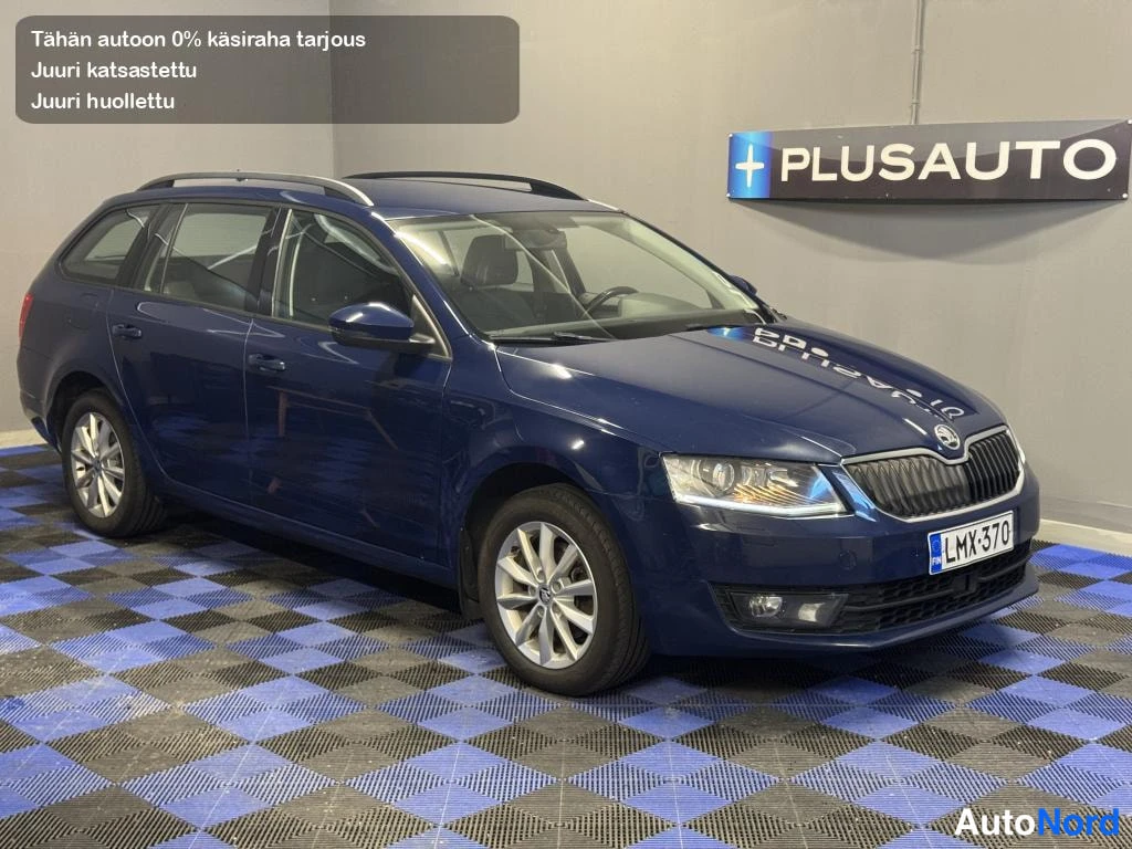 Etuviisto, nokka oikealle: Tummansininen farmariauto etuosalta ja oikealta sivulta sisätiloissa, kattokaiteet ja hopeavanteet näkyvät.