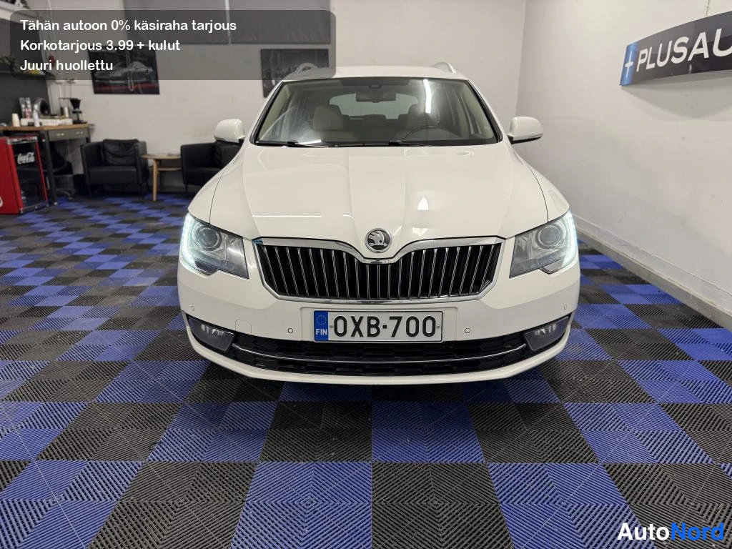 Edestä: Skoda Superbin etunäkymä suoraan edestä, ajovalot päällä, valkoinen koritakki.