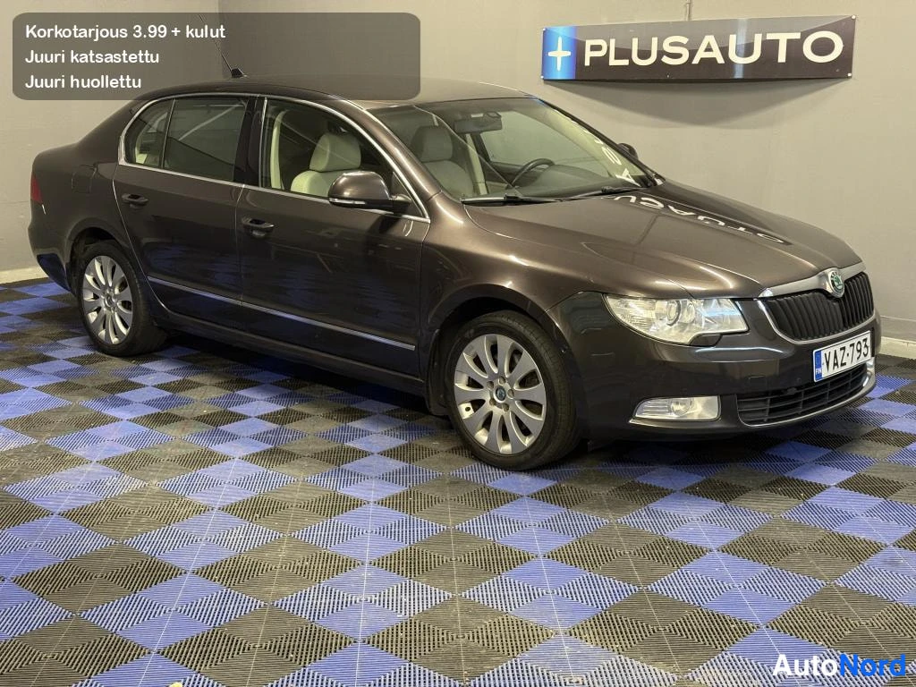 Etuviisto, nokka oikealle: Tummanruskea sedan-auto sisätiloissa etukulmasta oikealta kuvattuna, kevytmetallivanteet näkyvissä.