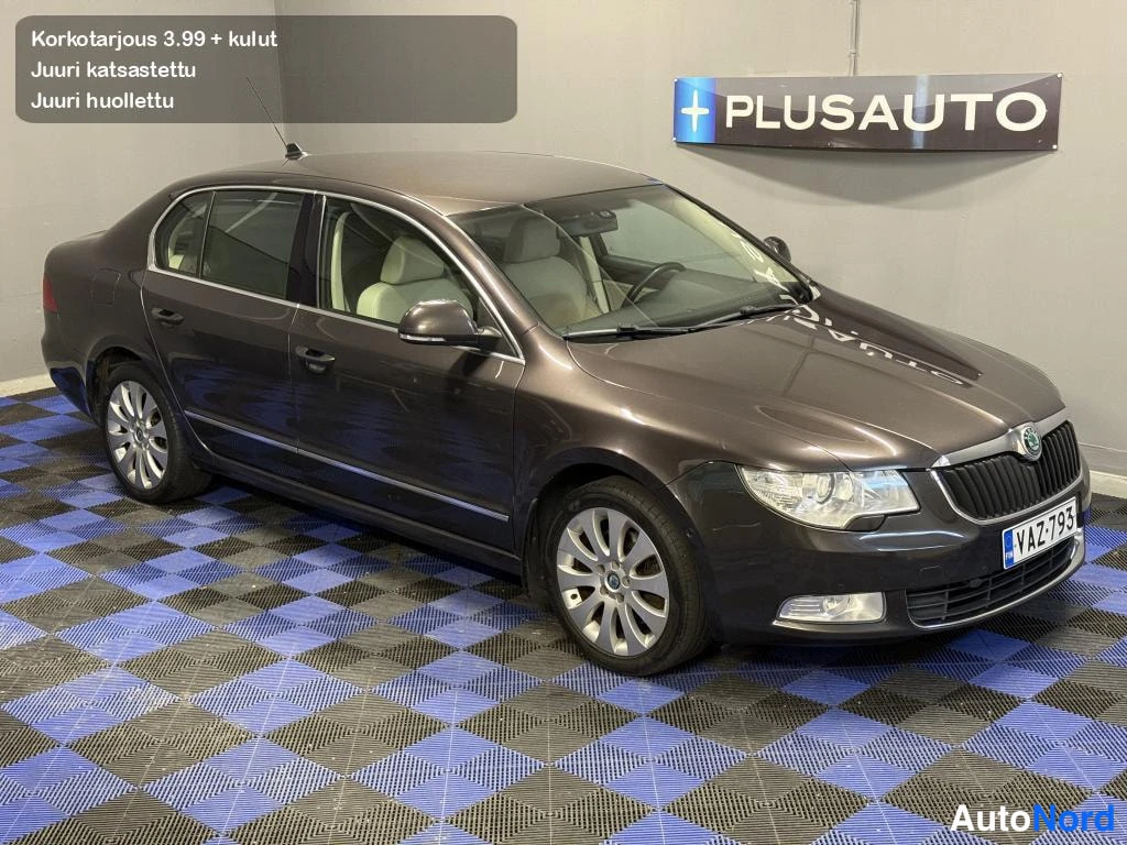 Etuviisto, nokka oikealle: Tummanruskea sedan-auto sisätiloissa etukulmasta oikealta kuvattuna, vaalea sisusta osittain näkyvissä ikkunoiden läpi.